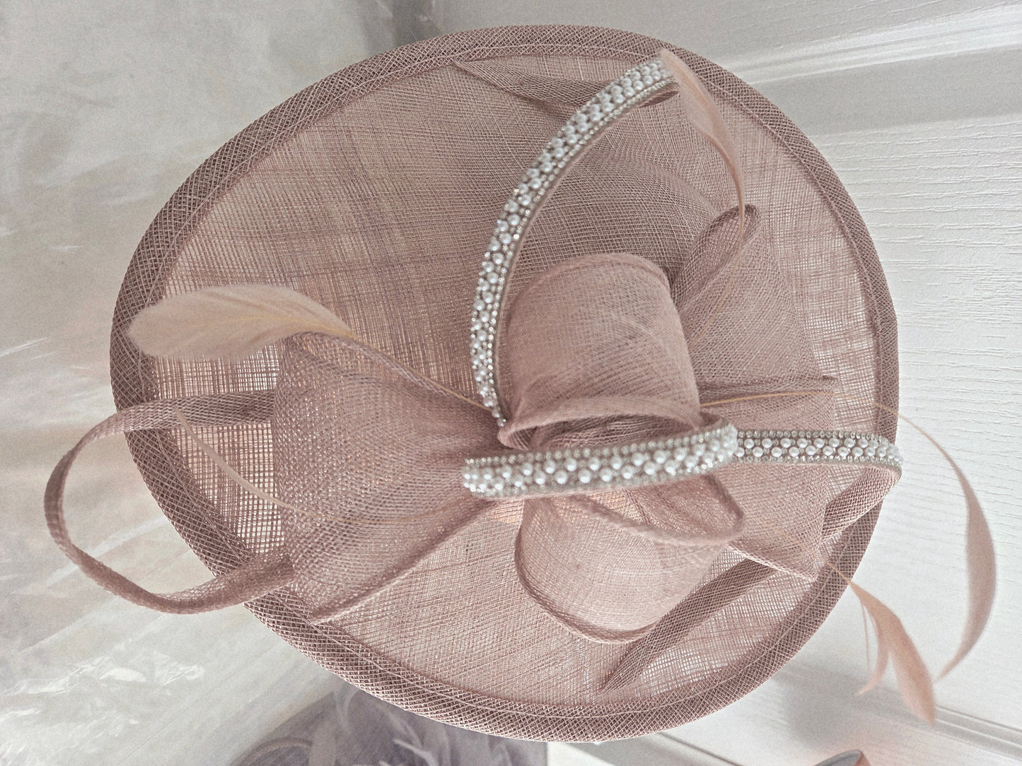 a pink taupe embellished fascinator hat with a blurred outdoor background
