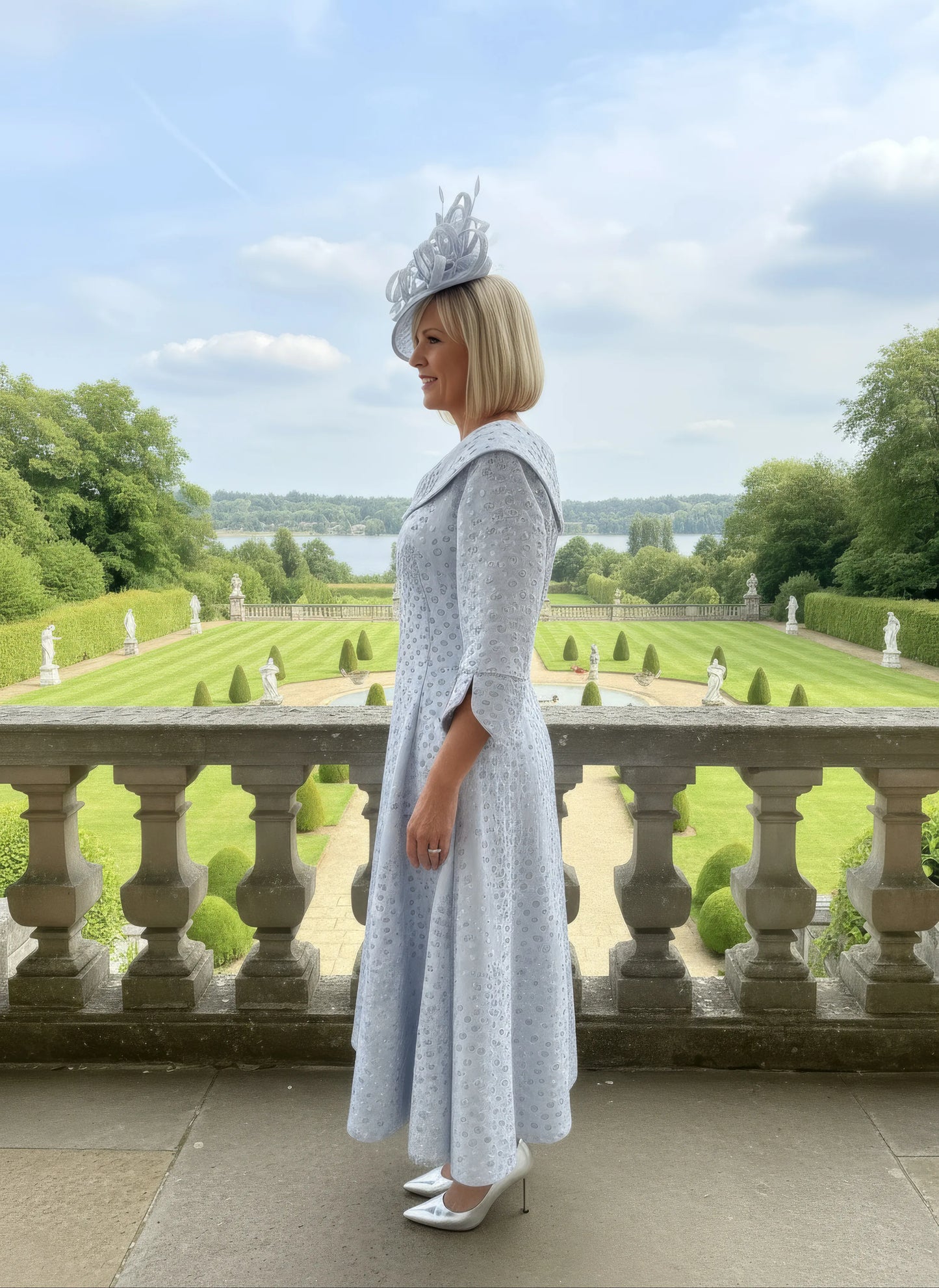 Woman in a light blue lizabella dress with a matching hat standing in a formal garden setting.