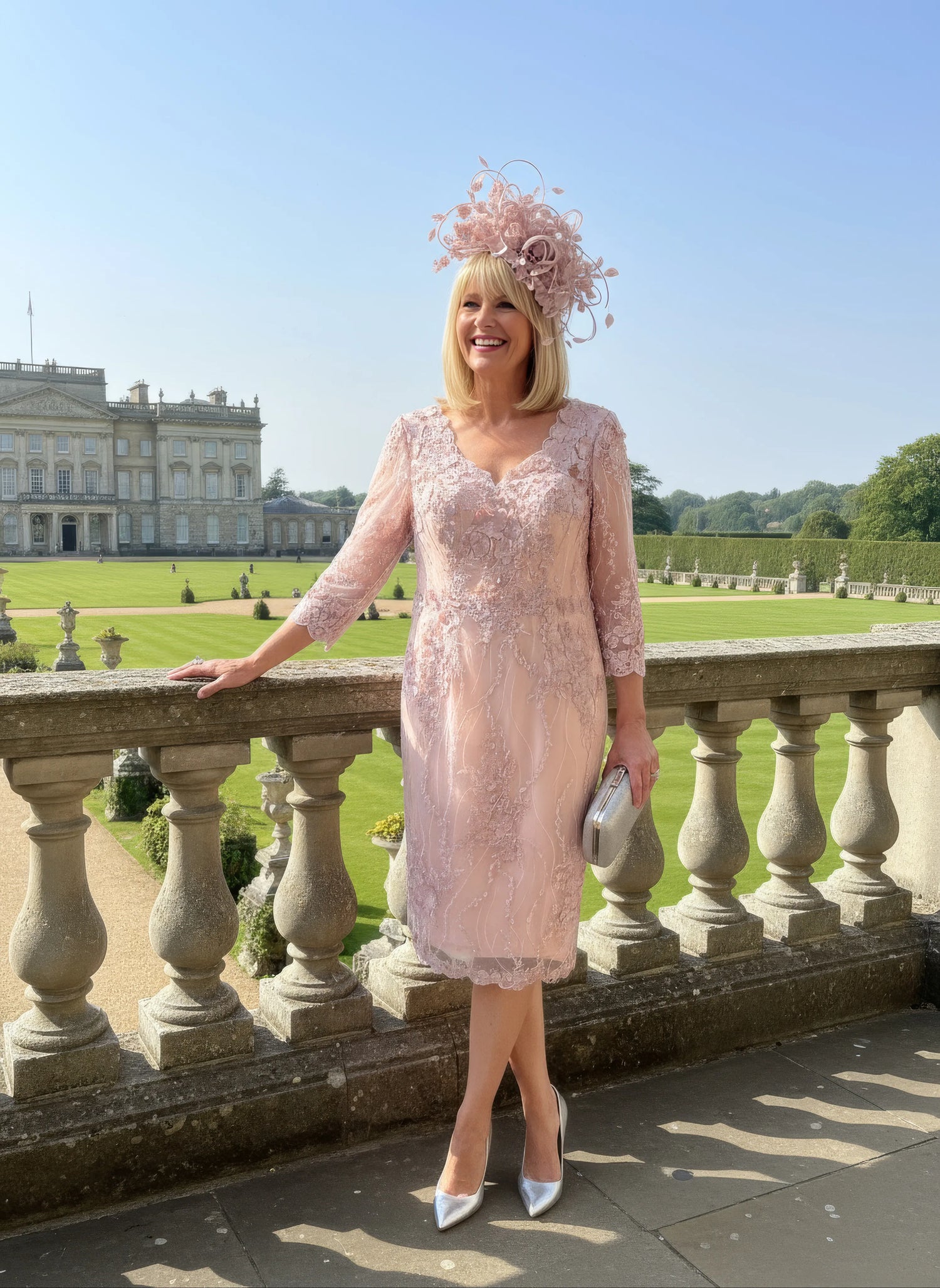 Woman in a light pink veni infantino v neck dress and hat standing on a stone balcony