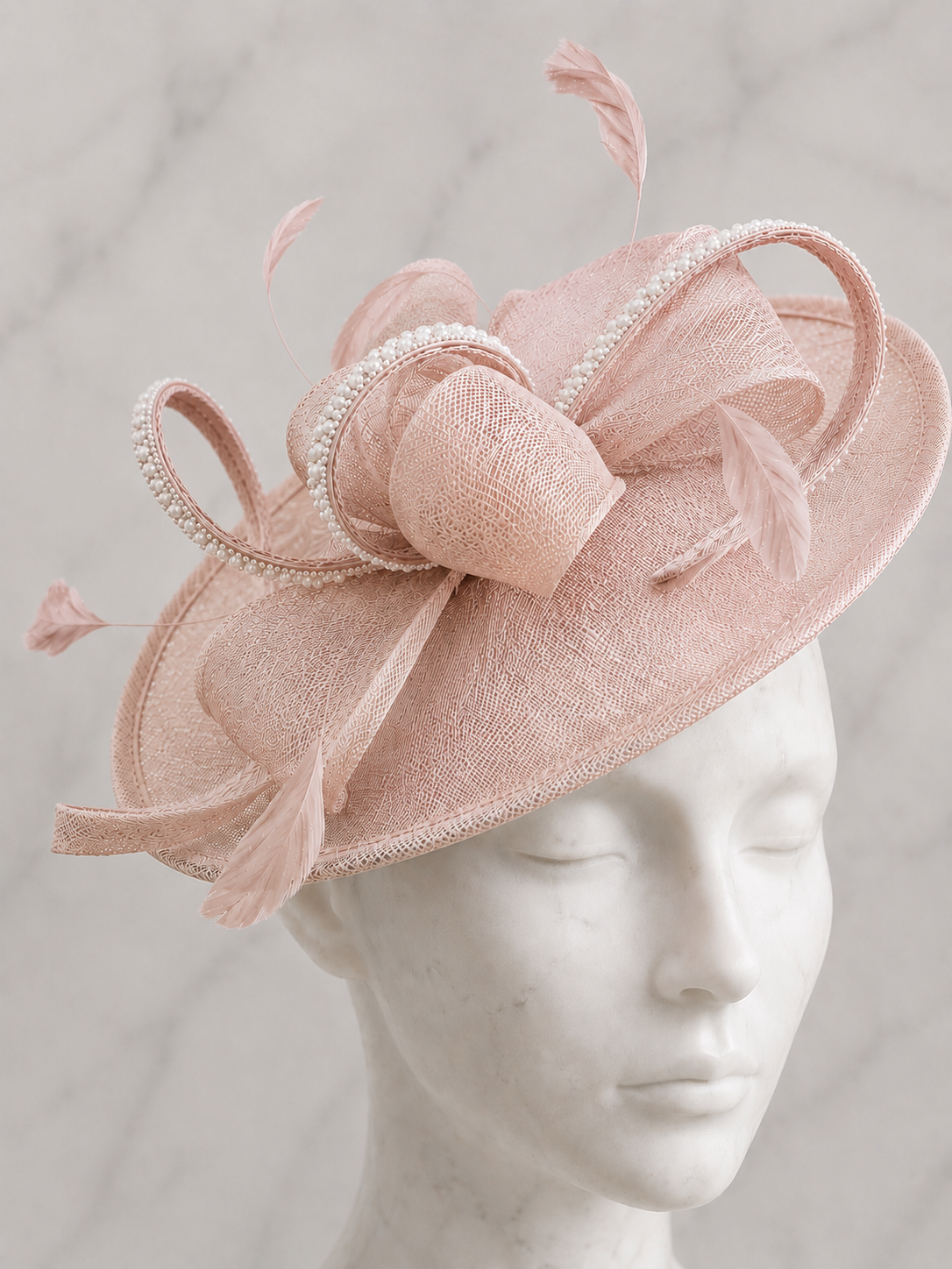 A Mother of the Bride pale pink fascinator embellished hat with feathers, rhinestones and pearls on a mannequin head