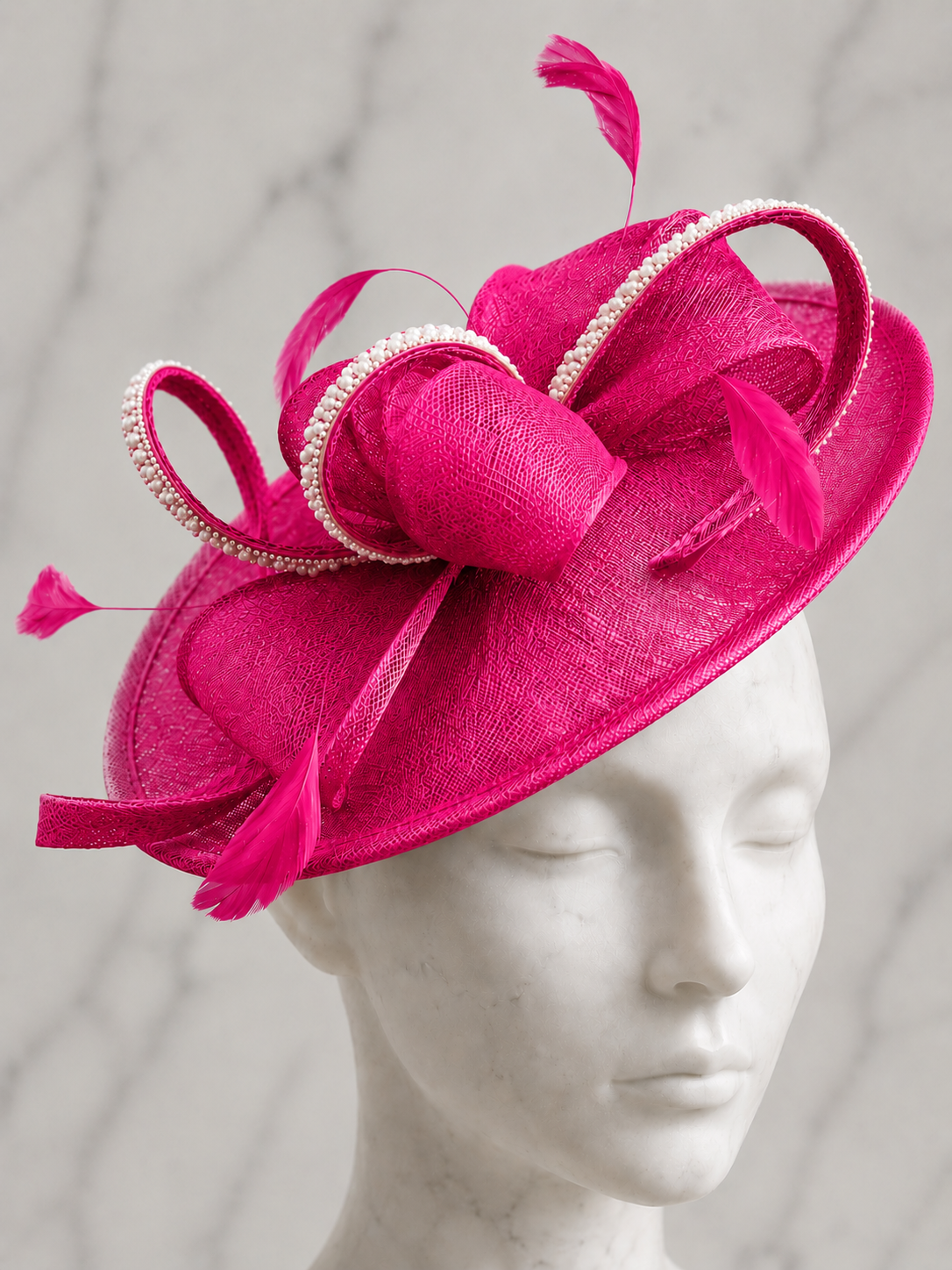A Mother of the Bride pale pink fascinator embellished hat with feathers, rhinestones and pearls on a marble head.