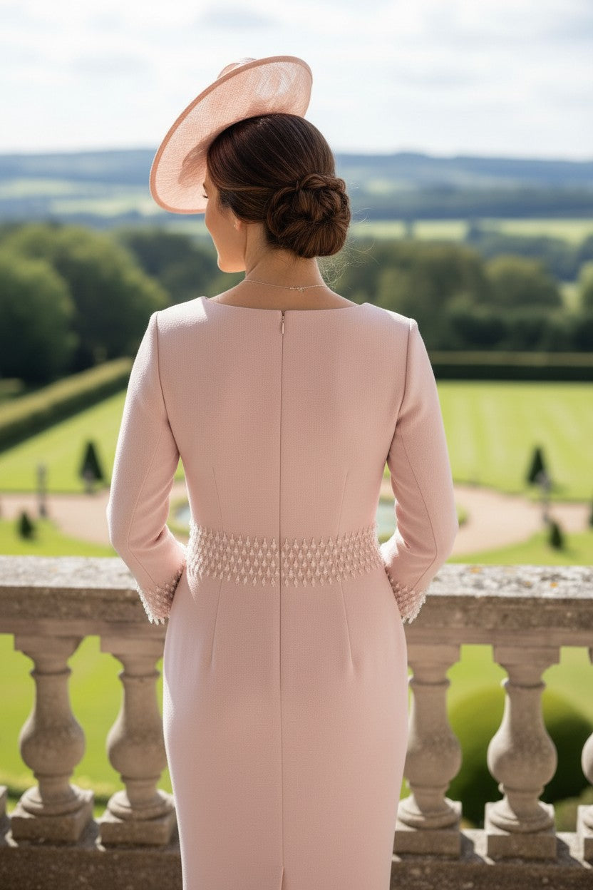 Woman in a pink mother of the bride dress and pink fascinator hat overlooking a scenic landscape