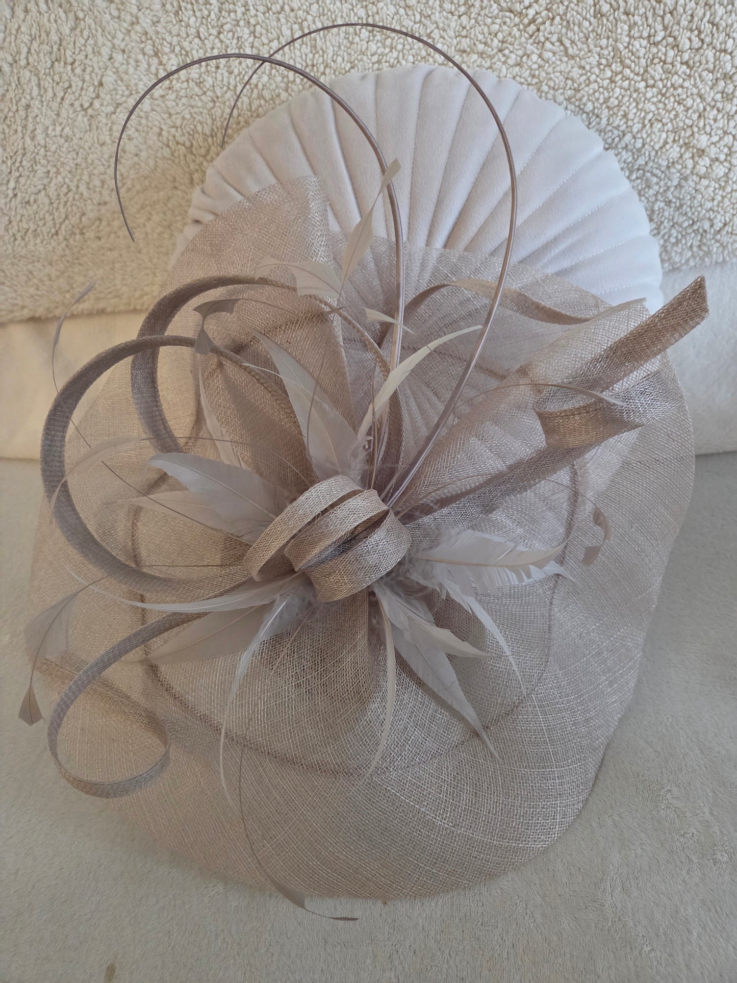 Beige feathered fascinator headpiece on a textured surface