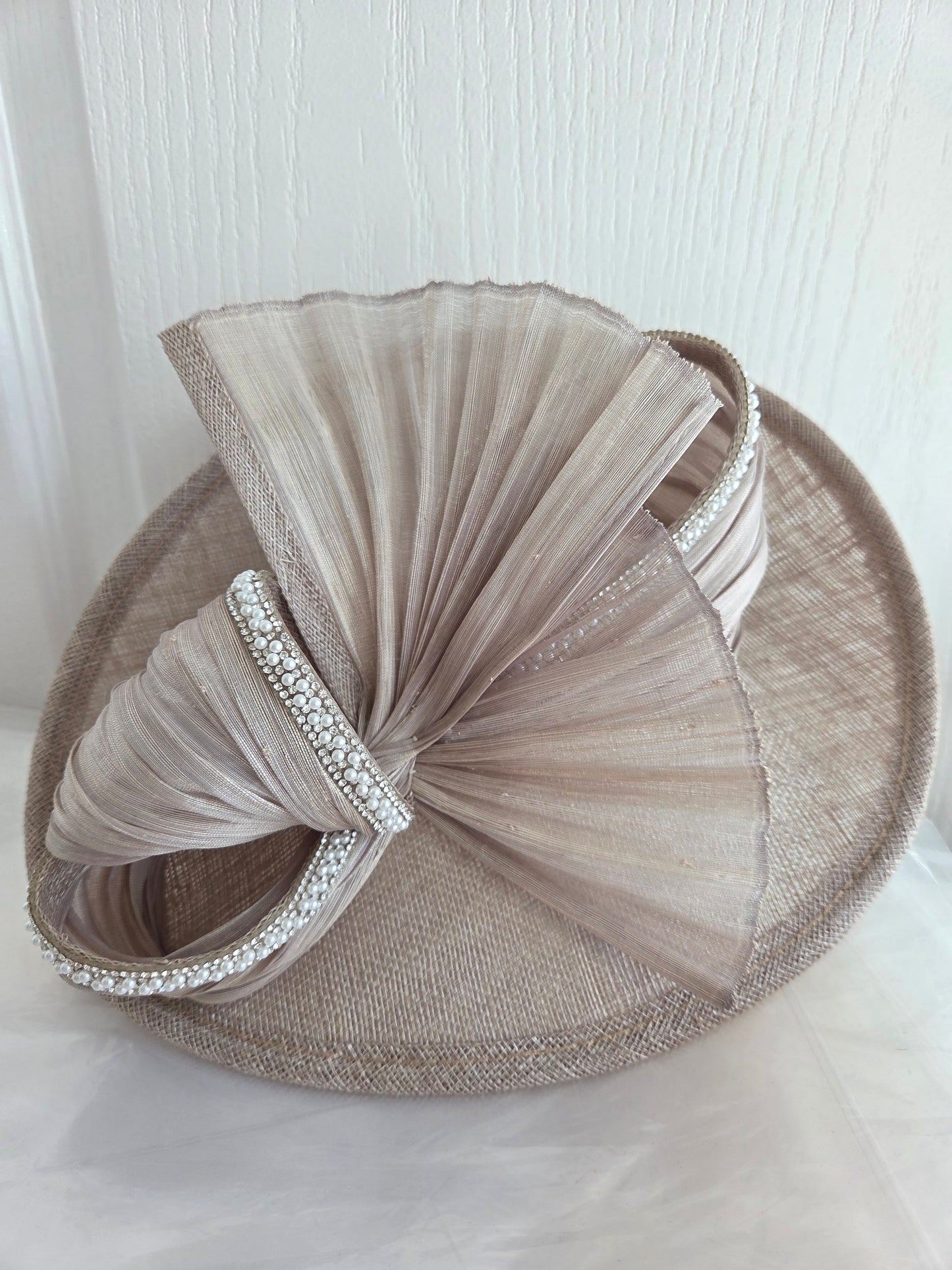 Beige fascinator with tulle and embellishments on a white background