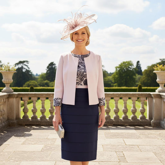 The Condici dress and jacket set in grey and blush pink boasts a flattering layered skirt. The ensemble features a lace bodice with elbow-length sleeves and is complemented by a contrasting jacket adorned with lace cuffs.