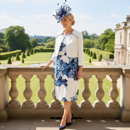 Elegant navy Mother of the Bride outfit by Condici 70820 featuring a fitted ruched dress with a coordinating cropped jacket, worn on a stone balcony overlooking manicured gardens.
