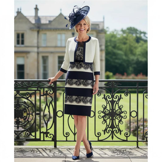 Woman in a floral condici navy and green mother of the bride dress and jacket she is also wearing a matching navy bespoke fasciantor hat standing on a balcony with a scenic background. Signature Dress.