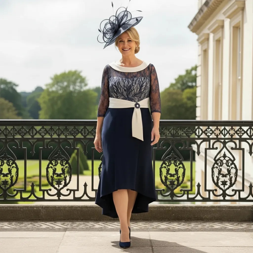 Navy and ivory Couture Club high‑low dress with lace bodice and 3/4 sequin sleeves, worn with a matching fascinator on a terrace.