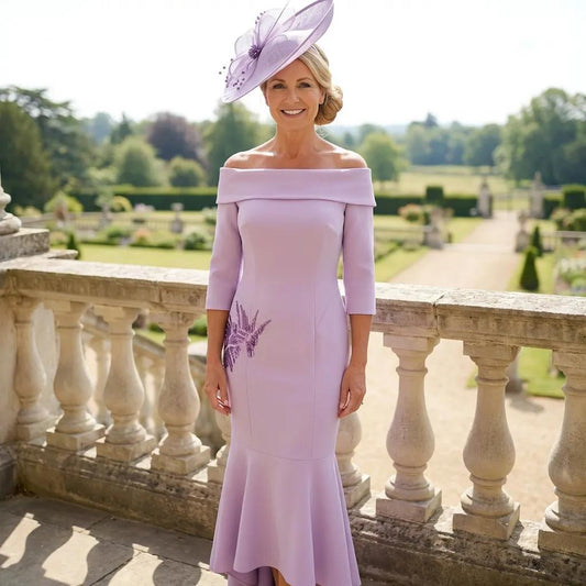 Lavender purple Couture Club 8G150 dress with off‑shoulder neckline, three‑quarter sleeves and side embellishments, shown on a stone balcony overlooking formal gardens.