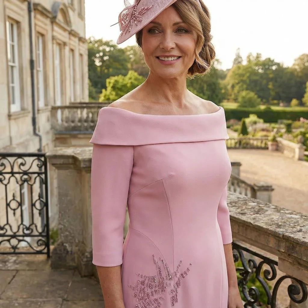 Couture Club 8G150 blush pink dress with off‑shoulder neckline and three‑quarter sleeves, shown on a stone terrace with a grand building behind.