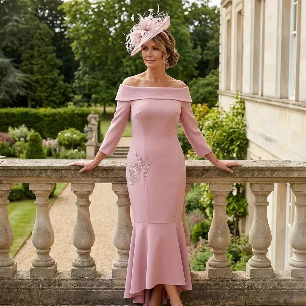 Blush pink Couture Club 8G150 dress with off‑shoulder neckline, three‑quarter sleeves and side embellishments, shown on a terrace overlooking formal gardens.