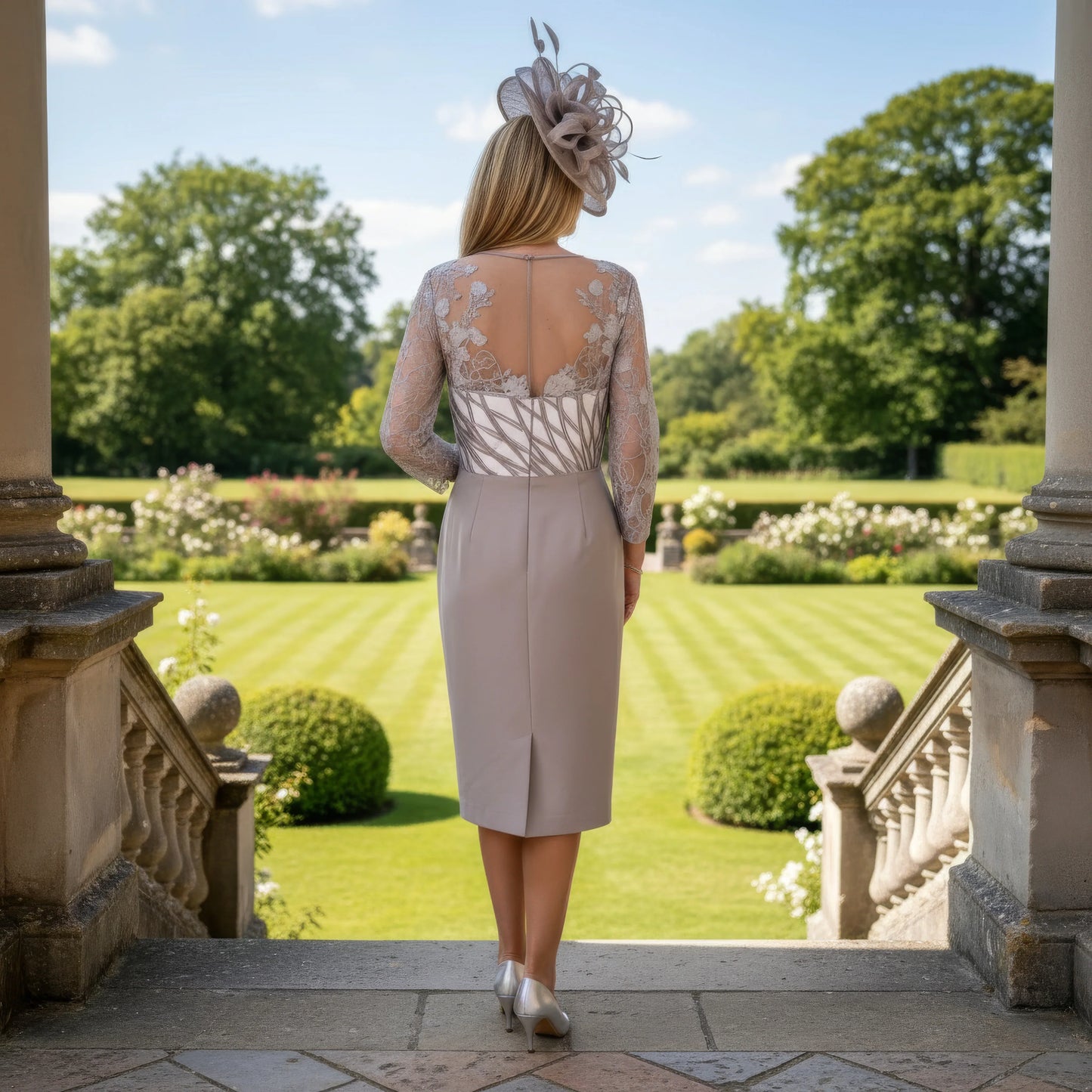 Woman in formal Dress in taupe colour by couture club. standing on a balcony with a grand building and garden