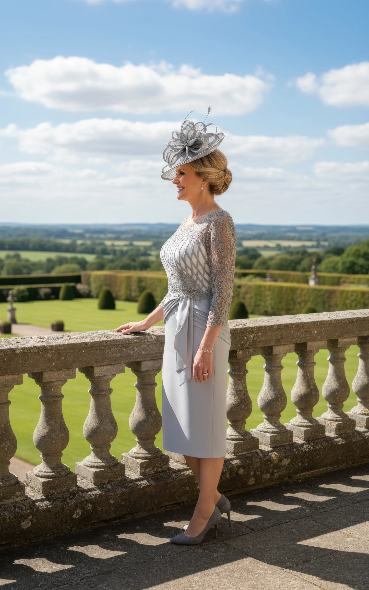 Woman in a stylish Silver grey mother of the bride dress and hat standing on a balcony with a scenic 