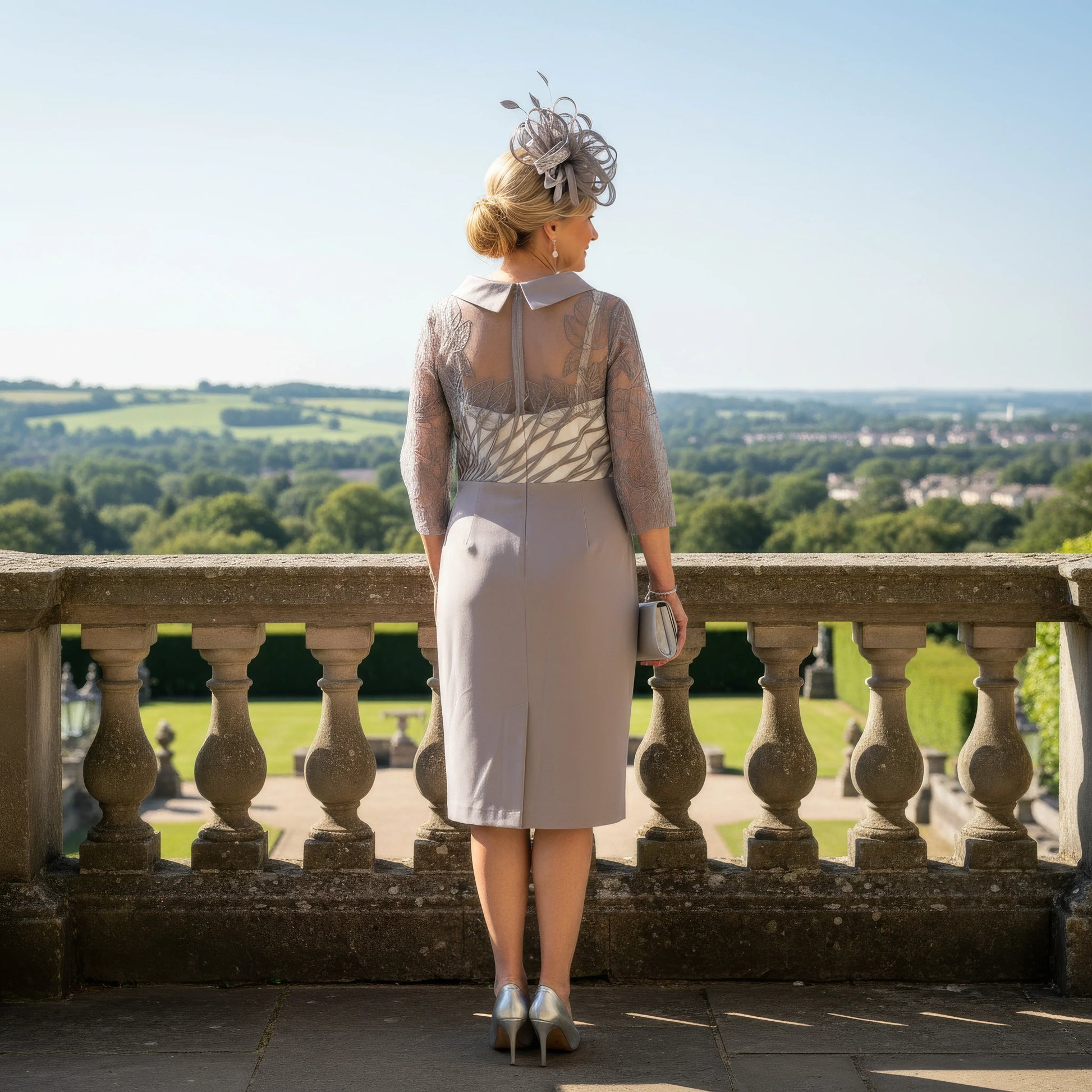 Woman in a light taupe Couture Club Mother of the Bride dress standing on a balcony ready to attend a wedding