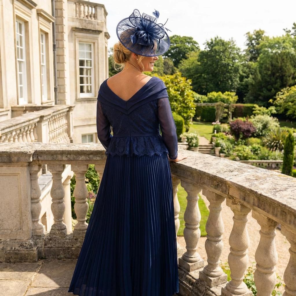 Woman in a Gill Harvey navy mother of the bride dress with a matching navy fascinator hat standing in a garden setting. Signature Dress.