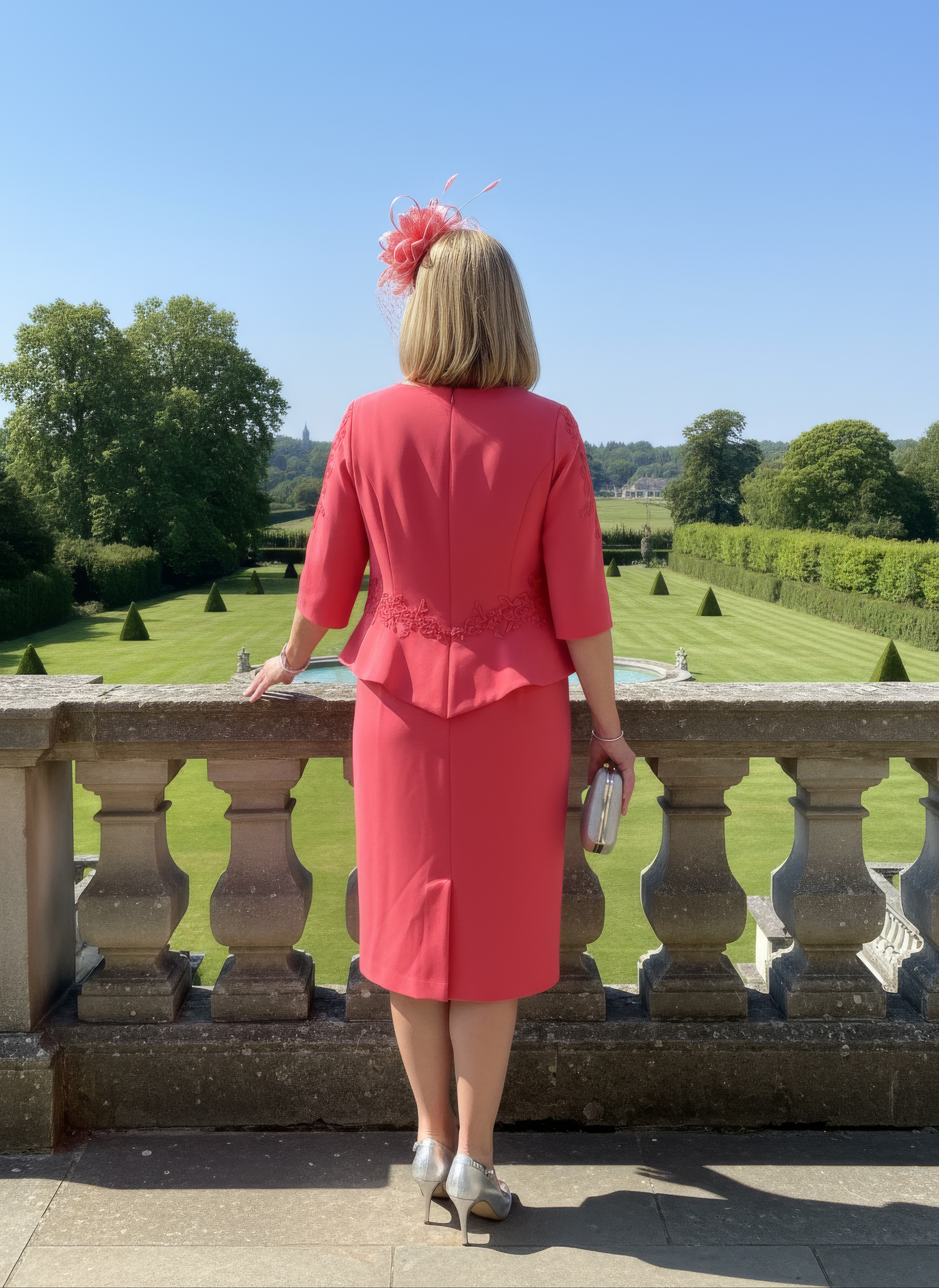 Woman in a pink outfit standing on a balcony overlooking a garden.