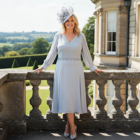 Woman in a light grey Lizabella Mother of the bride dress and hat standing on a balcony with a scenic background