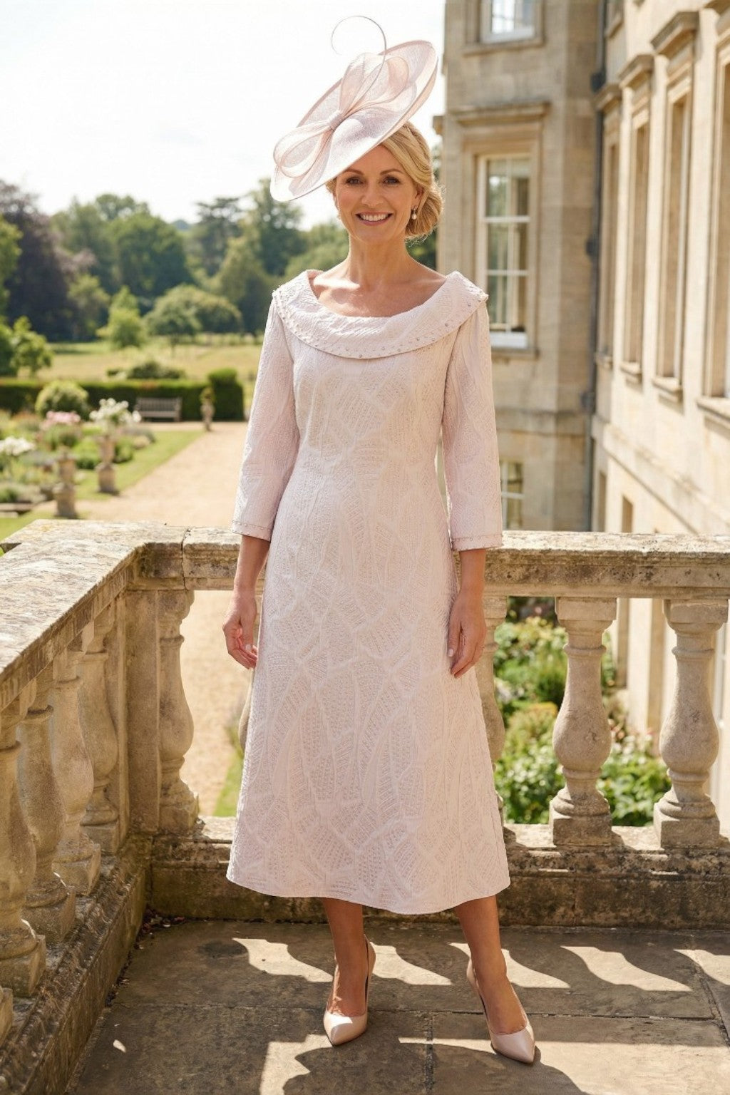 Woman stood wearing a lizabella light pink mother of the bride dress dress in an outdoor setting