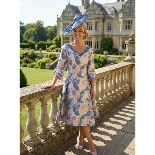 Lizabella 2515 blue and gold mother of the bride dress in metallic brocade with beaded V‑neckline and long sleeves, photographed outdoors at a stately venue.