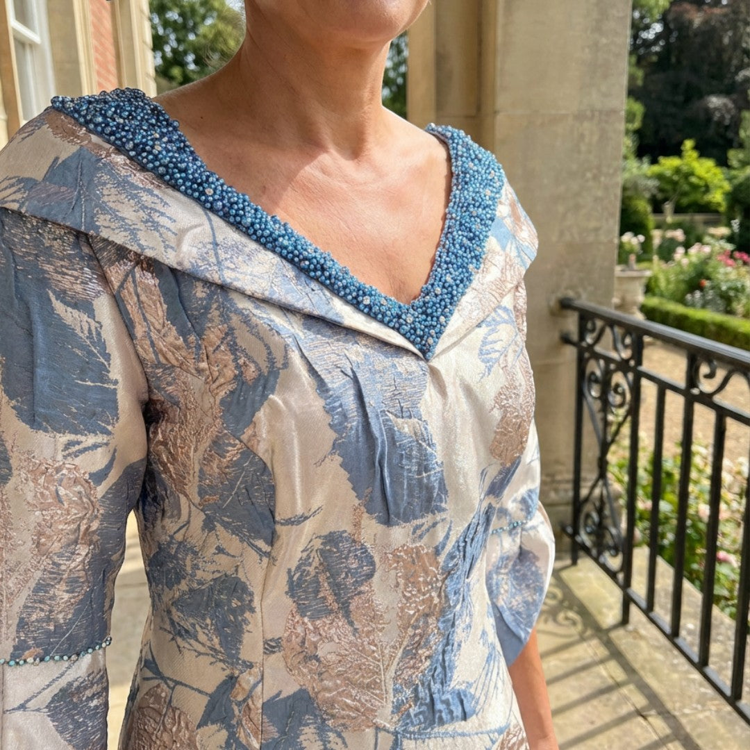 Lizabella 2515 blue mother of the bride dress in metallic brocade with matching hat, showing the elegant fit, beaded neckline and Autumn Winter styling