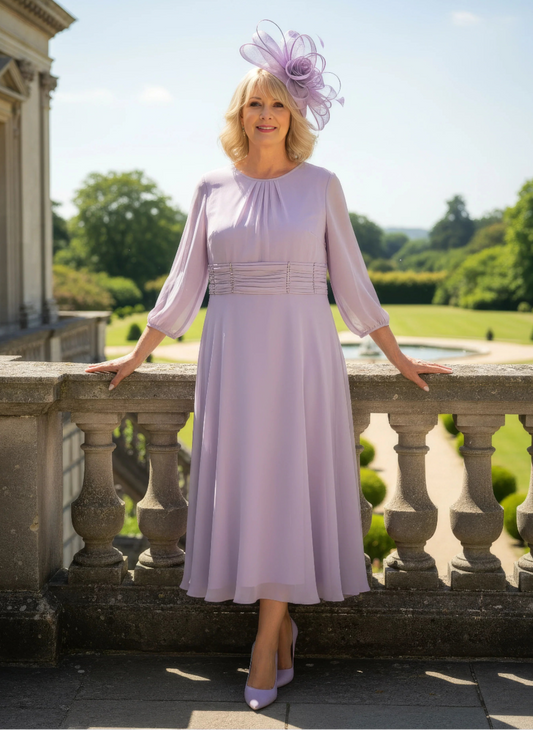 Woman in a light purple dress with a matching facinator hat standing on a stone balcony with a garden and building in the background.