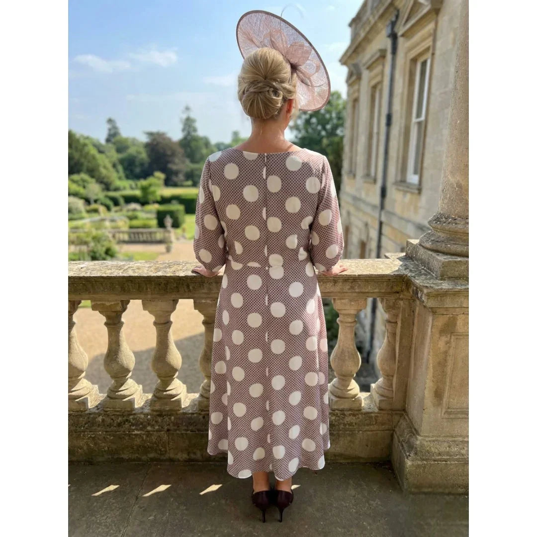 Woman in a Lizabella polka dot taupe mother of the bride dress and taupe fascinator standing on a balcony with a scenic view.
