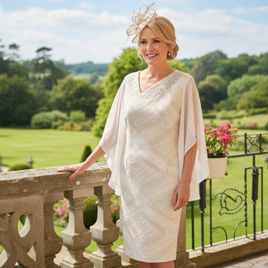 Woman in a Lizabella Champagne mother of the bride dress standing on a balcony with a scenic background. Signature Dress.