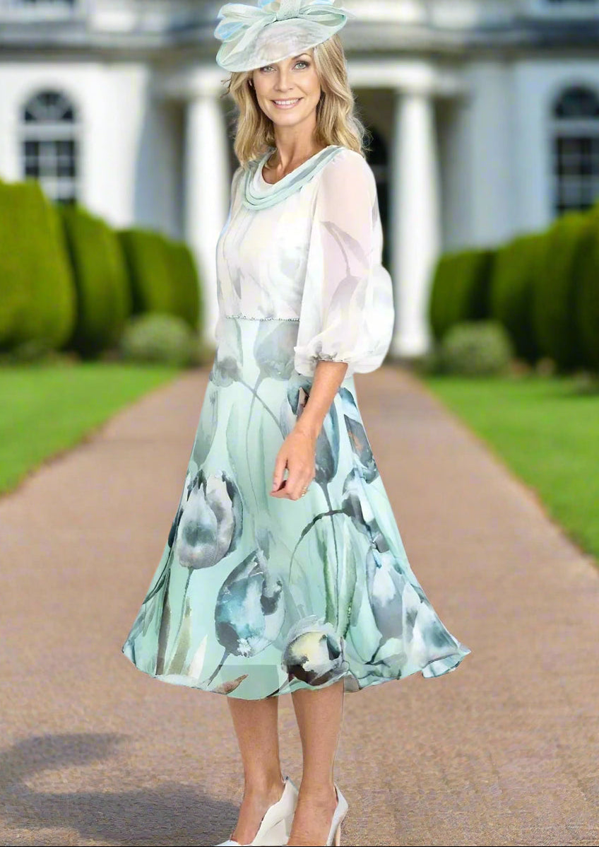 Lizabella dress in ice green and ivory floral chiffon fabric. Features draped neckline, 3/4 sleeves, and full skirt. Waist adorned with diamante detail.