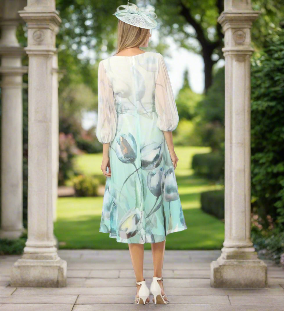 Lizabella dress in ice green and ivory floral chiffon fabric. Features draped neckline, 3/4 sleeves, and full skirt. Waist adorned with diamante detail.