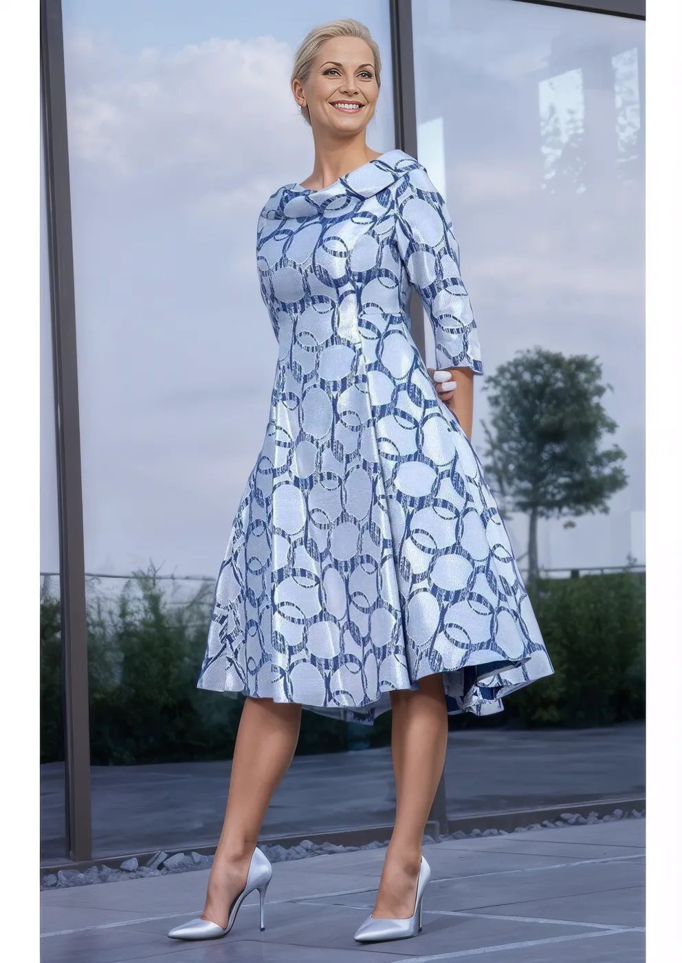 Fit and flare dress has a concealed zip to the back, lined, slip pockets to side, 3/4 sleeve and a full skirt in a metallic silver with navy circle print.