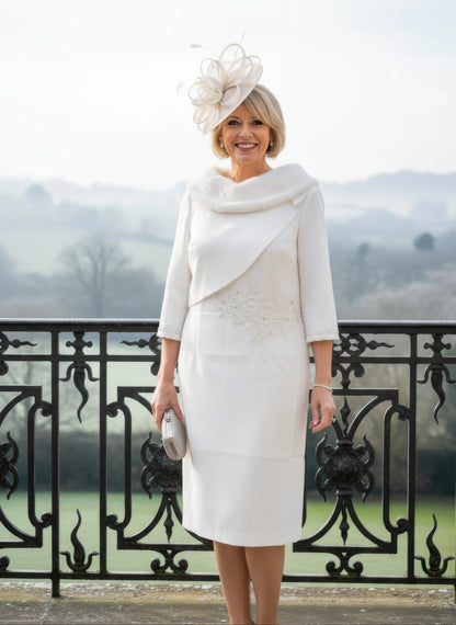 Woman in a white fur bridal dress with a matching hat standing on a balcony with a scenic background.