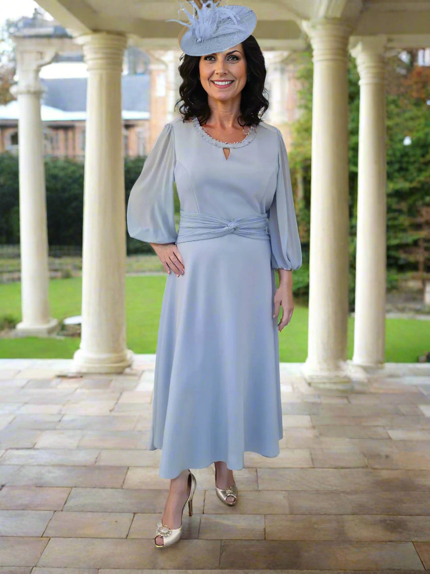 This stylish dress by Lizabella with a round neckline with inset v and bead detail has a voile 3/4 sleeve and pleat detail to waistline. The A Line style skirt completes the very flattering style.