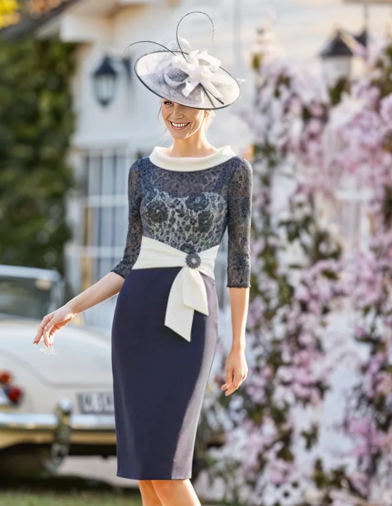 A Navy Ivory Dress with lace bodice and ivory boat neckline.

Elbow length sleeves and a sash waist with pearl embellished broach detailing.

The dress has a concealed zip to the back, lined and has an embellished broach to the front, long sleeved lace material