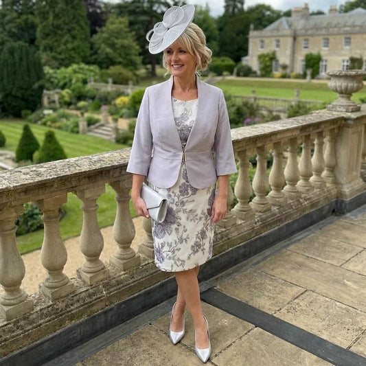 Woman in a Sonia Pena Silver formal mother of the bride outfit standing on a stone balcony with a garden and building in the background. Signature Dress.