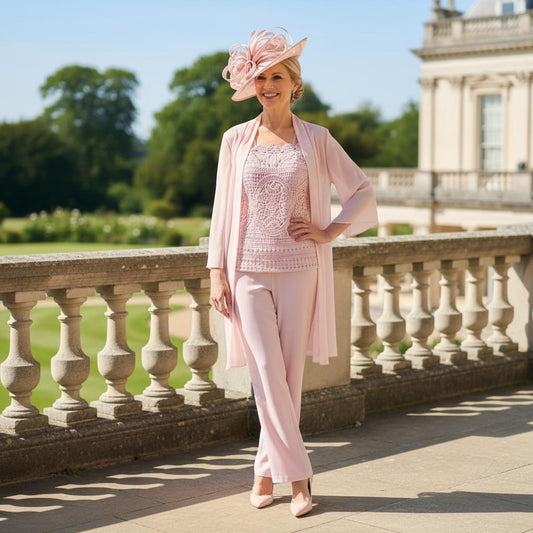 Woman in a veni infantino pink mother of the bride outfit standing on a stone pathway with greenery and a building in the background. Signature Dress.