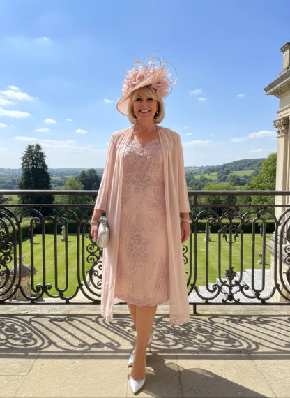 Woman in a light pink veni infantino v neck dress and hat standing on a stone balcony