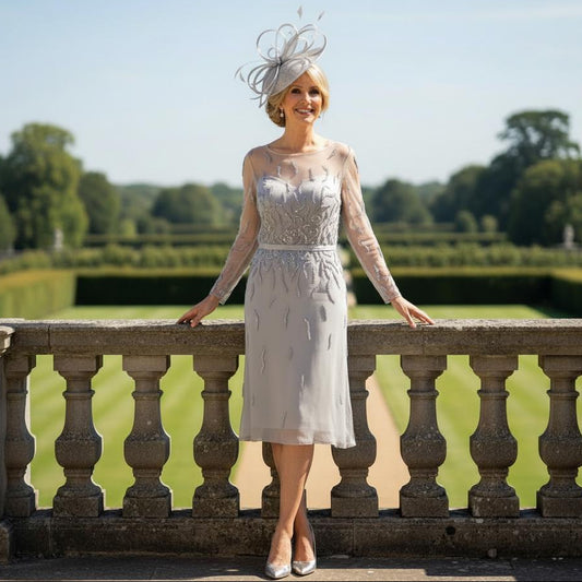 Woman in a Veni Infantino Silver gatsby mother of the bride dress and matching fascinator hat standing on a stone railing with a scenic background.  Signature Dress.