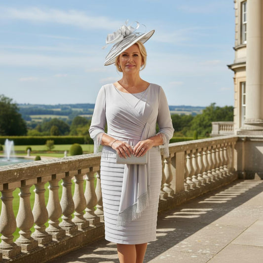 Plus Size Woman in a Dressed up Veromia  light gray Mother of the bride dress and matching fascinator standing on a balcony with a scenic background. Signature Dress.