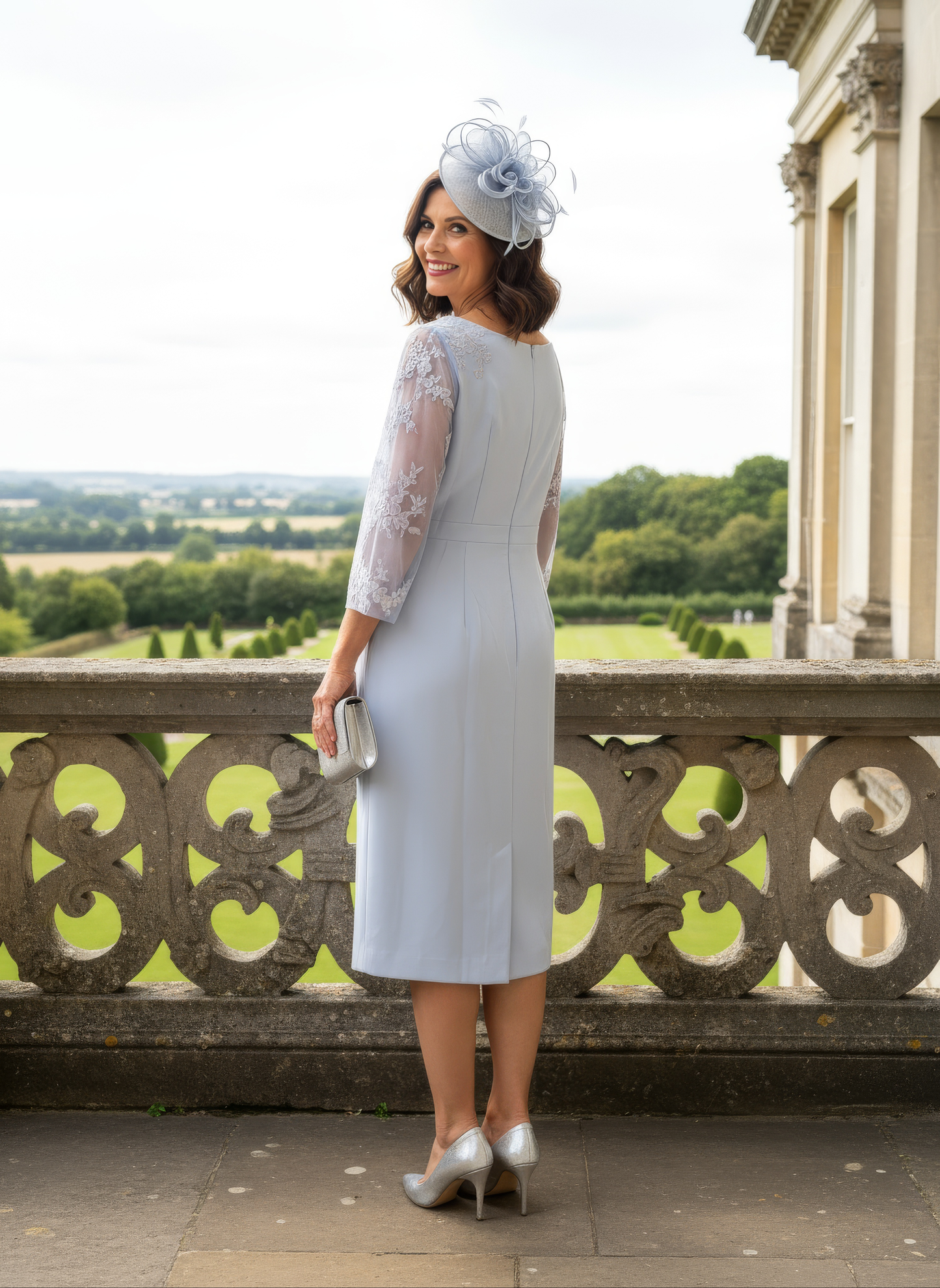 Woman in a light blue dress with lace sleeves standing on a balcony with a scenic view.