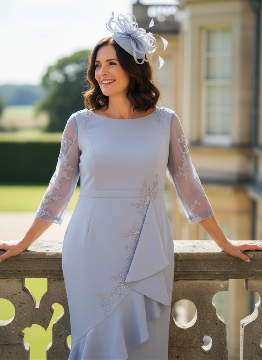 Woman in a light blue dress with lace sleeves and a matching headpiece standing outdoors.