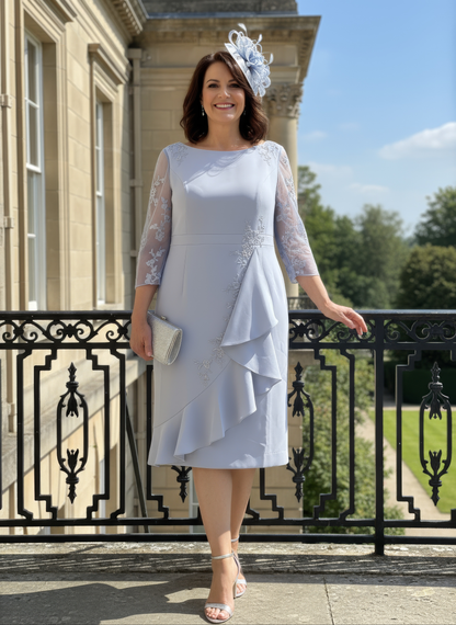 Woman in a light blue dress standing on a balcony with a building and greenery in the background