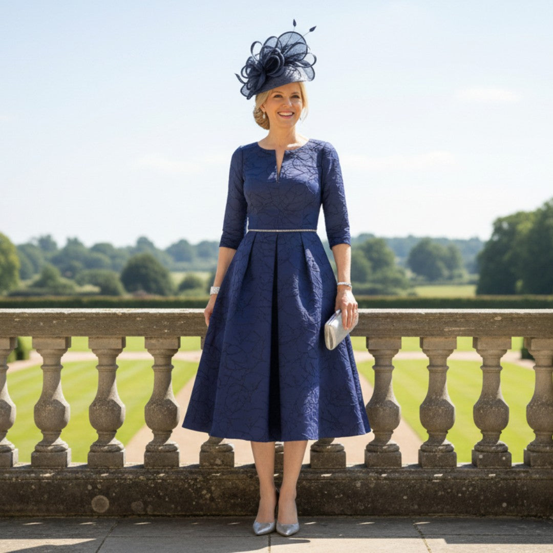 woman wearing a navy mother of the bride dress 3/ sleeve and embellished rhinestones along the waist, she is wearing as mother of the bride. Signature dress