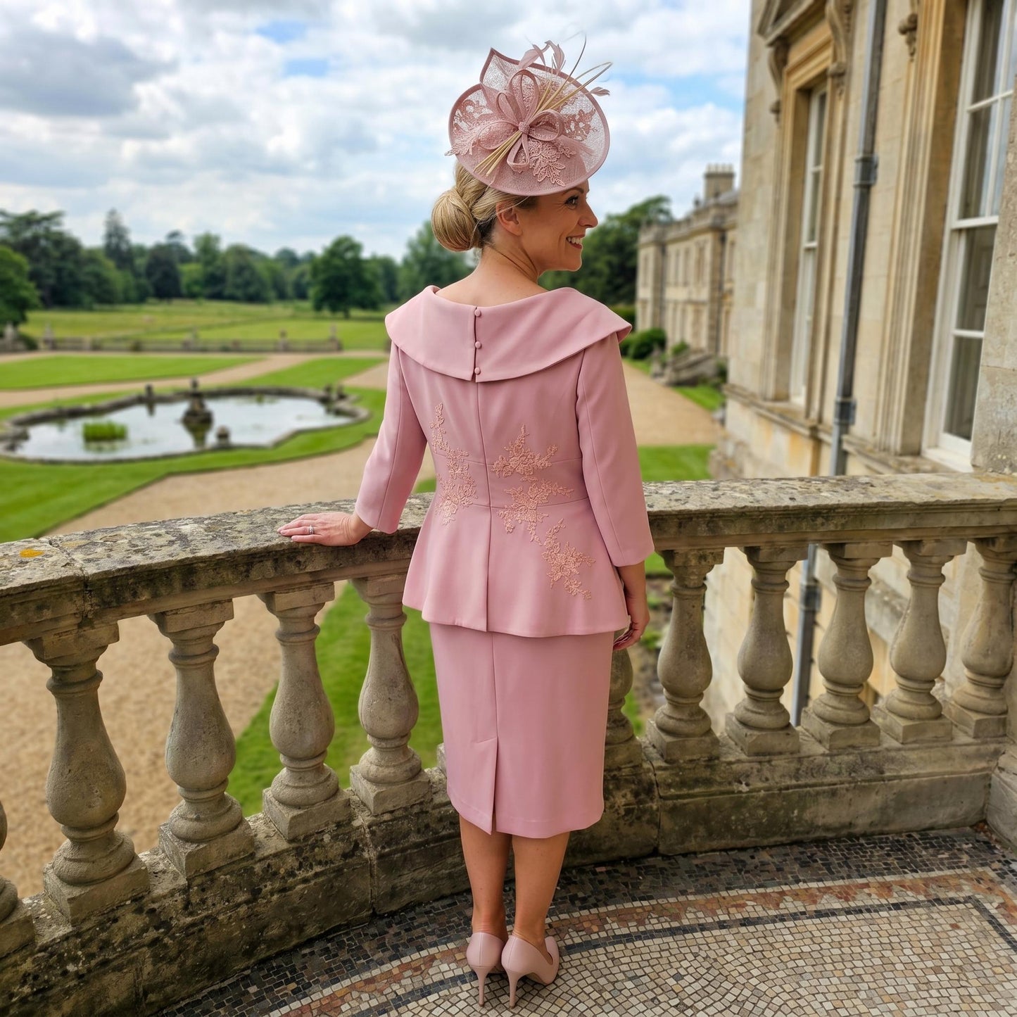Woman in a curvy pink mother of the bride dress by Veromia with a large building and garden in the background