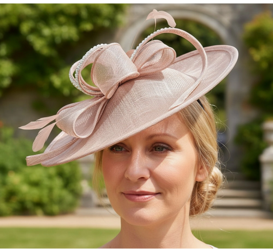Woman wearing a blush pink embellished fascinator hat with a blurred outdoor background