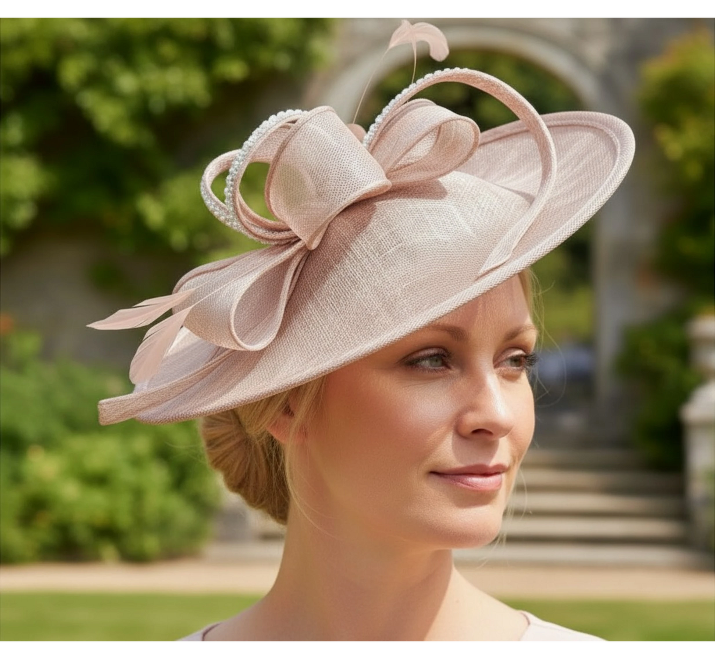 Woman wearing a blush pink embellished fascinator hat with a blurred outdoor background