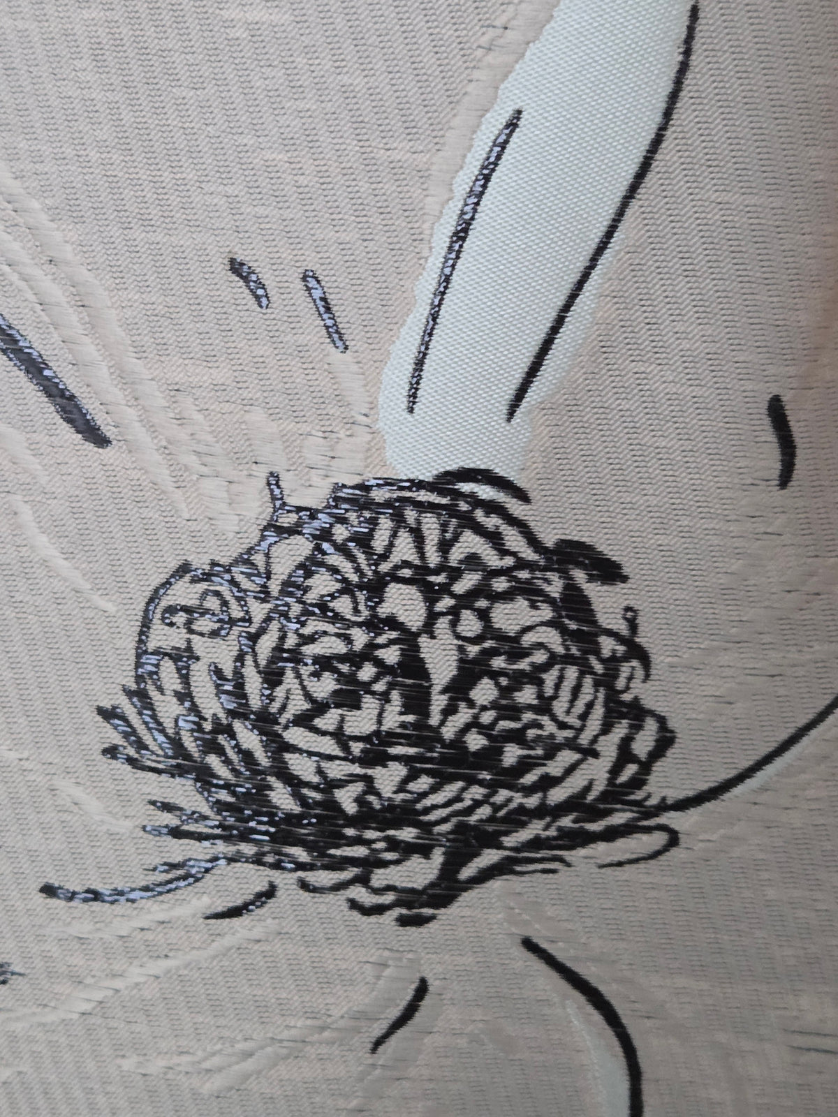 Close-up of a textured taupe gold fabric featuring a black embroidered sketch of a bird, likely a duck or goose, with a detailed circular body and simple curved wing lines.
