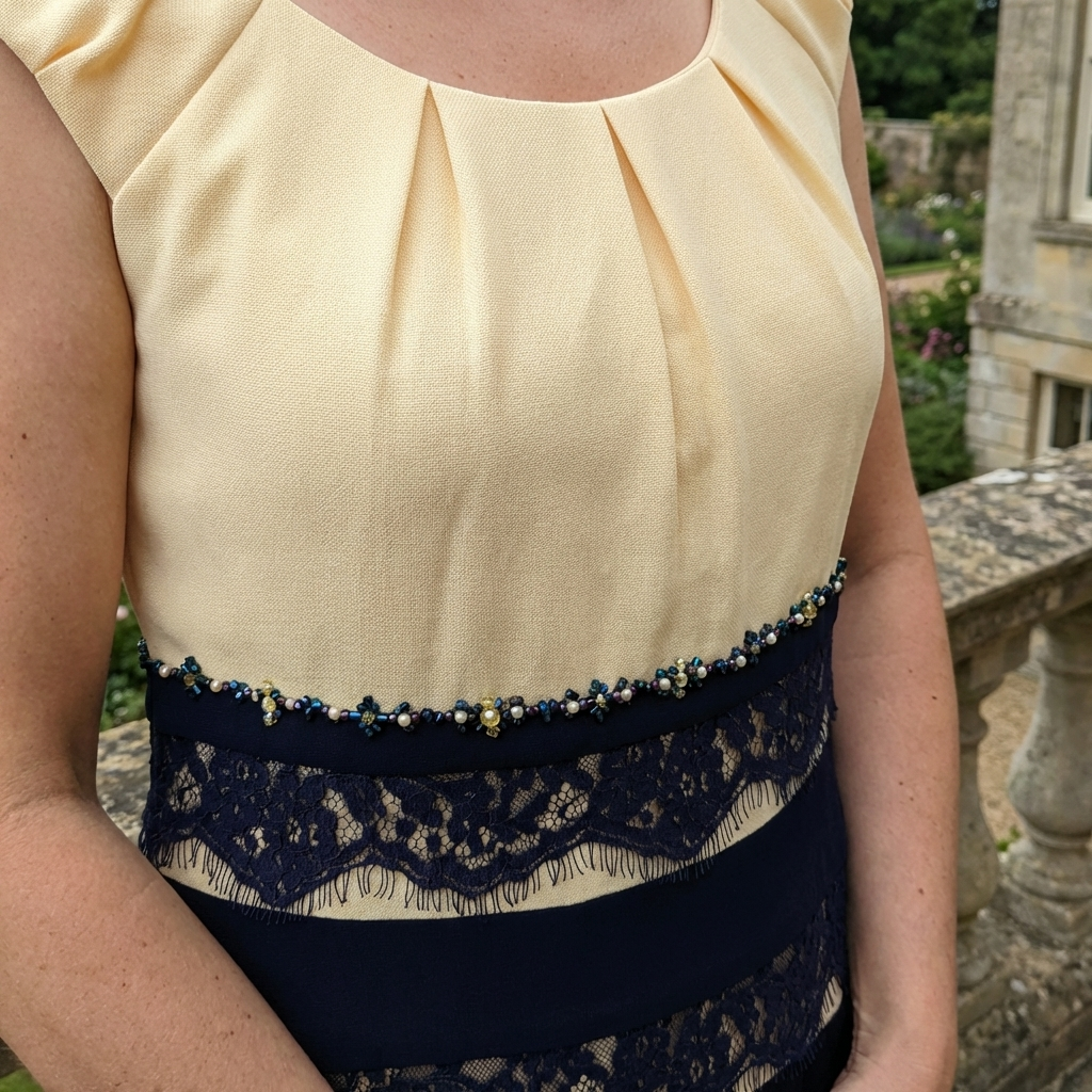 Close-up of Condici 70852 lemon dress showing beaded waist detail and pleated neckline.