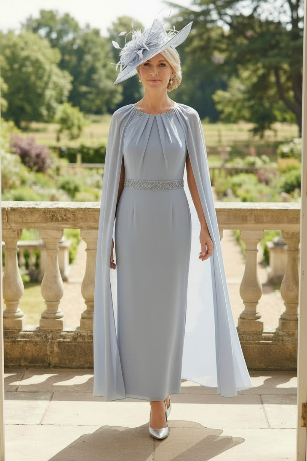 Rosa Clara Couture Club 8G151 blueâ€‘grey mother of the bride dress with flowing chiffon cape sleeves, embellished neckline and waist detail, shown outdoors on a stone terrace.