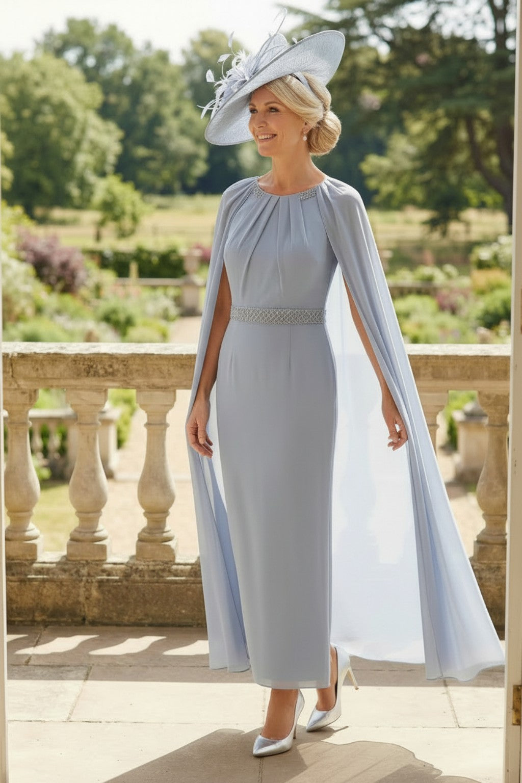 Rosa Clara Couture Club 8G151 blueâ€‘grey mother of the bride dress with flowing chiffon cape sleeves and embellished waistband, photographed outdoors against a garden backdrop.