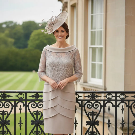 Woman in elegant taupe dress and oval taupe embellished fascinator hat standing on a balcony with a scenic background